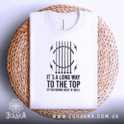 Футболка для рокера, біла, складена на плетеній основі, фон світлий, принт чорного кольору з текстом "IT'S A LONG WAY TO THE TOP (IF YOU WANNA ROCK 'N' ROLL)" та графічними елементами.