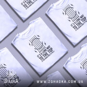 Футболка для рокера, біла, зображена на манекені, фон світлий, принт чорного кольору з текстом "IT'S A LONG WAY TO THE TOP (IF YOU WANNA ROCK 'N' ROLL)" та графічними елементами у вигляді струни та блискавок.