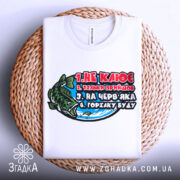 Футболка для риболовлі, білого кольору, зображена зверху на плетеному кошику, фон нейтральний, принт з рибою та текстом, видно комір футболки.