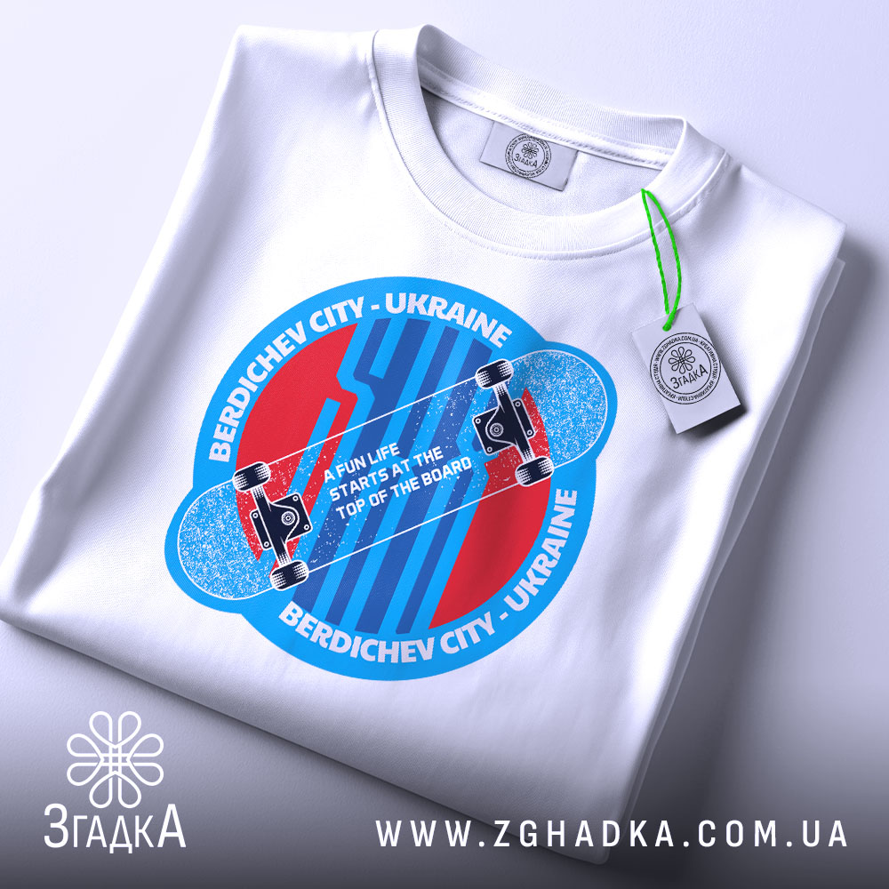 Футболка для скейтера, білого кольору, зображена на столі, фон світлий, принт аналогічний попередньому, з додатковою етикеткою зеленого кольору.