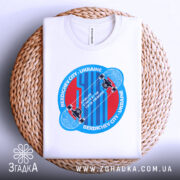 Футболка для скейтера, білого кольору, складена на плетеній кошику, фон нейтральний, принт аналогічний попереднім, з акцентом на текстуру тканини.