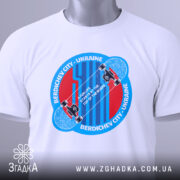 Футболка для скейтера, білого кольору, зображена на столі, фон світлий, принт аналогічний попередньому, з додатковою етикеткою зеленого кольору.