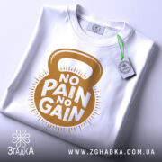 Футболка для спортсменів, біла, складена на столі, фон світло-сірий, принт з написом 'NO PAIN NO GAIN' у золотистому кольорі, з етикеткою зеленого кольору.