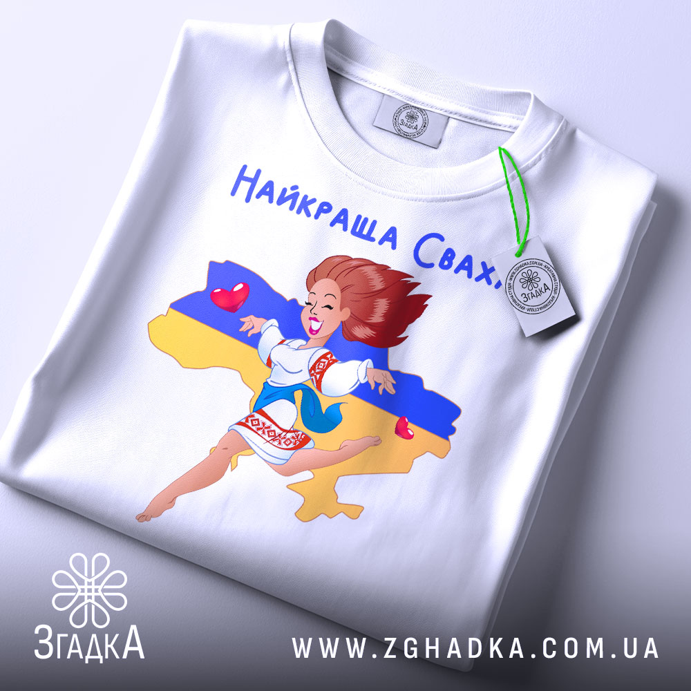 Футболка для свахи білого кольору, складена на столі, фон світлий, принт з дівчиною в українському вбранні, зображена на фоні карти України, з прикріпленою етикеткою.