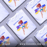 Футболка для свахи білого кольору, зображена з фронтального ракурсу на манекені, фон нейтральний, принт з веселою дівчиною в українському вбранні на фоні карти України з жовтою та синьою смугами.