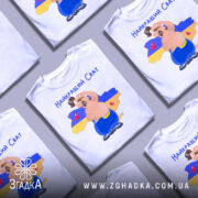 Футболка для свата, біла, зображена на манекені, фон нейтральний, принт з веселим персонажем на фоні карти України, текст 'Найкращий Сват' зверху, сердечка на карті.