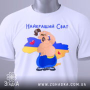 Футболка для свата, біла, складена на поверхні, фон нейтральний, принт з веселим персонажем на фоні карти України, текст 'Найкращий Сват' зверху, етикетка на рукаві.