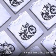 Футболка для велосипедиста, білого кольору, зображена на манекені, фон світлий, принт з чорним малюнком велосипеда на фоні лісу з деревами.