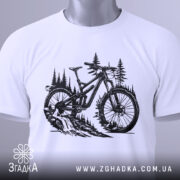 Футболка для велосипедиста, білого кольору, складена на поверхні, фон світлий, принт з чорним малюнком велосипеда на фоні лісу, з етикеткою зеленого кольору.