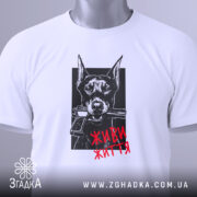 Футболка доберман живи життя, біла футболка на столі, зображення добермана з пістолетом у пащі на чорному фоні, текст 'ЖИВИ ЖИТТЯ' червоним кольором, етикетка з зеленим шнурком.