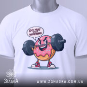 Футболка донат спорт мотивація, складена біла футболка з принтом веселого пончика, що піднімає штангу, текст 'DO NUT STOP WORKING' над принтом, на фоні світло-сірого кольору, з етикеткою зеленого кольору.