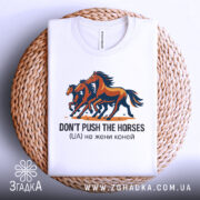 Футболка don't push the horses, білого кольору, складена на плетеній кошику, фон світло-сірий, принт з трьома конями, кольори принта - коричневий, чорний та оранжевий, текст під принтом чорного кольору.