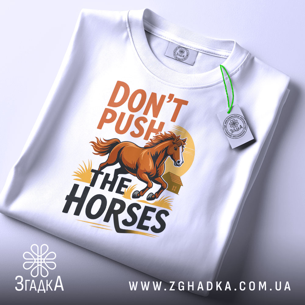 Футболка don't push the horses білого кольору, складена на поверхні, з видимим етикеткою, фон світло-сірий, принт з конем та написом у верхній частині.