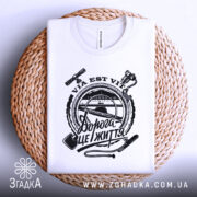 Футболка дорога це життя, складена біла футболка з чорним принтом, зображена на плетеній основі, фон білий, принт містить текст "Дорога це життя" та зображення інструментів.