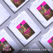 Футболка досконалість нудна, білого кольору, з фронтальним ракурсом, на манекені, фон нейтральний, принт з зображенням жінки з зеленим волоссям та написом 'ДОСКОНАЛІСТЬ НУДНА' яскраво-рожевого кольору.