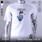 Футболка дружу з кукухою, біла, зображена на манекені з правого боку, фон світло-сірий, принт з малюнком вовка у блакитній футболці, який тримає кукурудзу, текст над малюнком українською мовою.