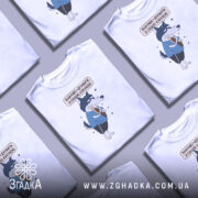 Футболка дружу з кукухою, біла, зображена на манекені з правого боку, фон світло-сірий, принт з малюнком вовка у блакитній футболці, який тримає кукурудзу, текст над малюнком українською мовою.