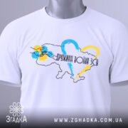 Футболка дружина воїна ЗСУ, білого кольору, складена на поверхні, фон світло-сірий, принт з контуром України, кольоровими серцями та написом, з етикеткою на комірці.