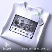 Футболка друзі письменники, біла, складена на поверхні, фон світло-сірий, принт з чорно-білою фотографією людей та написом 'FRIENDS' кольоровими літерами, з зеленим ярликом.