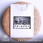Футболка друзі письменники, біла, складена на плетеній кошику, фон світло-сірий, принт з чорно-білою фотографією людей та написом 'FRIENDS' кольоровими літерами.
