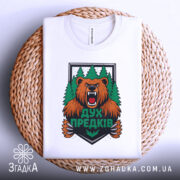 Футболка дух предків білого кольору, зображена зверху на плетеній основі, фон білий, принт з ведмедем та лісом яскравий, деталі принта чіткі.