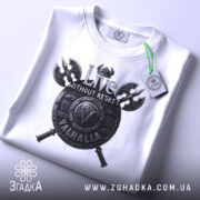 Футболка дух Вальгалли, біла, складена на поверхні, зображена зверху, фон світлий, принт з написом 'Live WITHOUT REGRET' та щитом, прикріплений етикет.