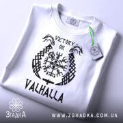 Футболка дух вікінга, біла, зображена зверху, на столі, фон світло-сірий, принт чорного кольору з написом 'VICTORY OR VALHALLA' та зеленим ярликом.
