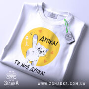 Футболка дупка ти моя, біла футболка, зображена зверху, принт з котом на жовтому фоні, текст "Дупка! Ти моя дупка!", з зеленим ярликом.