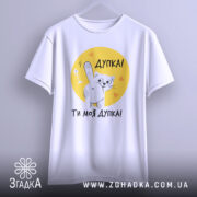 Футболка дупка ти моя, біла футболка з коротким рукавом, зображення кота, що показує лапкою, на жовтому фоні з сердечками, текст "Дупка! Ти моя дупка!" під принтом, фон світло-сірий.