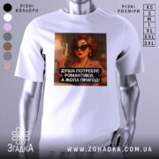 Футболка душа потребує романтики. Біла футболка з принтом, зображення жінки в чорних окулярах, яка тримає келих з шампанським, фон з м'яким освітленням. Принт містить текст: 'ДУША ПОТРЕБУЄ РОМАНТИКИ, А ЖОПА ПРИГОД!'