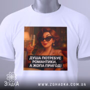 Футболка душа потребує романтики. Біла футболка, зображена зверху, принт з жінкою в чорних окулярах, яка тримає келих з шампанським. На футболці є етикетка з логотипом бренду. Текст принта: 'ДУША ПОТРЕБУЄ РОМАНТИКИ, А ЖОПА ПРИГОД!'