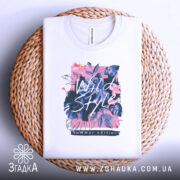 Футболка дикий стиль, біла, складена на плетеній кошику, фон світло-сірий, принт з квітами та написом 'Wild Style', видно етикетку на горловині.