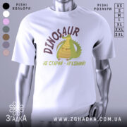 Футболка динозавр не старий. Білий колір, зображена з фронтального ракурсу на манекені. Фон світло-сірий, принт з веселим динозавром та написом 'НЕ СТАРИЙ - АРХІВНИЙ!' у коричневих тонах.