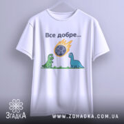 Футболка динозаври все добре. Біла футболка з коротким рукавом, зображена з фронтального ракурсу, підвішена на вішалці. На фоні світло-сірий градієнт. Принт з двома динозаврами, один зелений, інший блакитний, які дивляться на метеорит, що падає, з написом 'Все добре...' над ними.