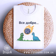 Футболка динозаври все добре. Біла футболка, складена на кошику, зображена з верхнього ракурсу. На фоні світло-сірий градієнт. Принт з двома динозаврами, один зелений, інший блакитний, які дивляться на метеорит, що падає, з написом 'Все добре...' над ними.