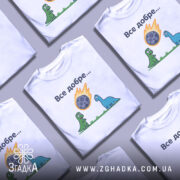 Футболка динозаври все добре. Біла футболка з коротким рукавом, зображена з фронтального ракурсу. На фоні світло-сірий градієнт. Принт з двома динозаврами, один зелений, інший блакитний, які дивляться на метеорит, що падає, з написом 'Все добре...' над ними.