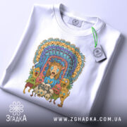 Футболка дивні істоти, складена на столі, фон світло-сірий, принт кольоровий, зображує дивних істот і обличчя, центральна фігура з рудим волоссям, на футболці є етикетка з зеленим шнурком.