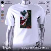 Футболка Джокер білого кольору, зображена на манекені з блискучою поверхнею, фон світло-сірий. Принт з обличчям Джокера з червоними губами та зеленим волоссям, деталі обличчя чітко видимі.