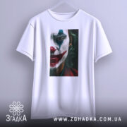 Футболка Джокер білого кольору, підвішена на вішалці, фон світло-сірий. Принт з обличчям Джокера, акцент на виразі обличчя та кольорах макіяжу.