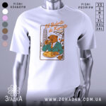 Футболка El Bobrito білого кольору, зображена на манекені, з принтом ведмедя в костюмі, який тримає піцу, на фоні архітектурних елементів.