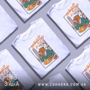 Футболка El Bobrito білого кольору, зображена на манекені, з принтом ведмедя в костюмі, який тримає піцу, на фоні архітектурних елементів.