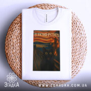 Футболка електро крик кіт білого кольору, зображена зверху на плетеному кошику, фон світлий, принт з чорним котом з великими жовтими очима на фоні абстрактного пейзажу.