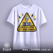 Футболка електрик був провідником. Біла футболка, підвішена на вішалці, з принтом у вигляді жовтого трикутника з чорним контуром, всередині якого зображений усміхнений скелет. Фон світло-сірий.
