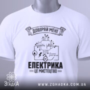 Футболка електрика мистецтво, біла, складена на поверхні, фон світло-сірий, принт чорного кольору з елементами електричних схем і написом 'ЕЛЕКТРИКА ЦЕ МИСТЕЦТВО', на комірці видна етикетка.