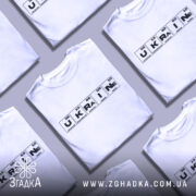 Футболка елементи України, біла, зображена на манекені, фон світло-сірий, принт з елементами таблиці Менделєєва, де слово 'UKRAINE' виділено чорним кольором.