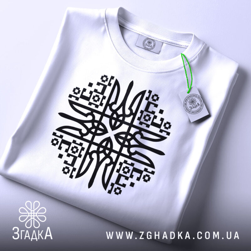 Футболка етно стиль, біла, складена на поверхні, фон світло-сірий, принт чорного кольору з геометричними елементами, на комірці є етикетка.