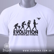 Футболка еволюція, біла, складена на столі, фон світло-сірий, принт чорного кольору з написом 'EVOLUTION ВІД ПЛІВКИ ДО ПУЛЬТА' та силуетами людей, що займаються різними видами зйомки, з етикеткою зеленого кольору.