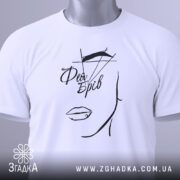 Футболка фея брів, білого кольору, складена на поверхні, фон світлий, принт з малюнком обличчя та написом 'Фея Брів' у чорному кольорі, з зеленим ярликом.