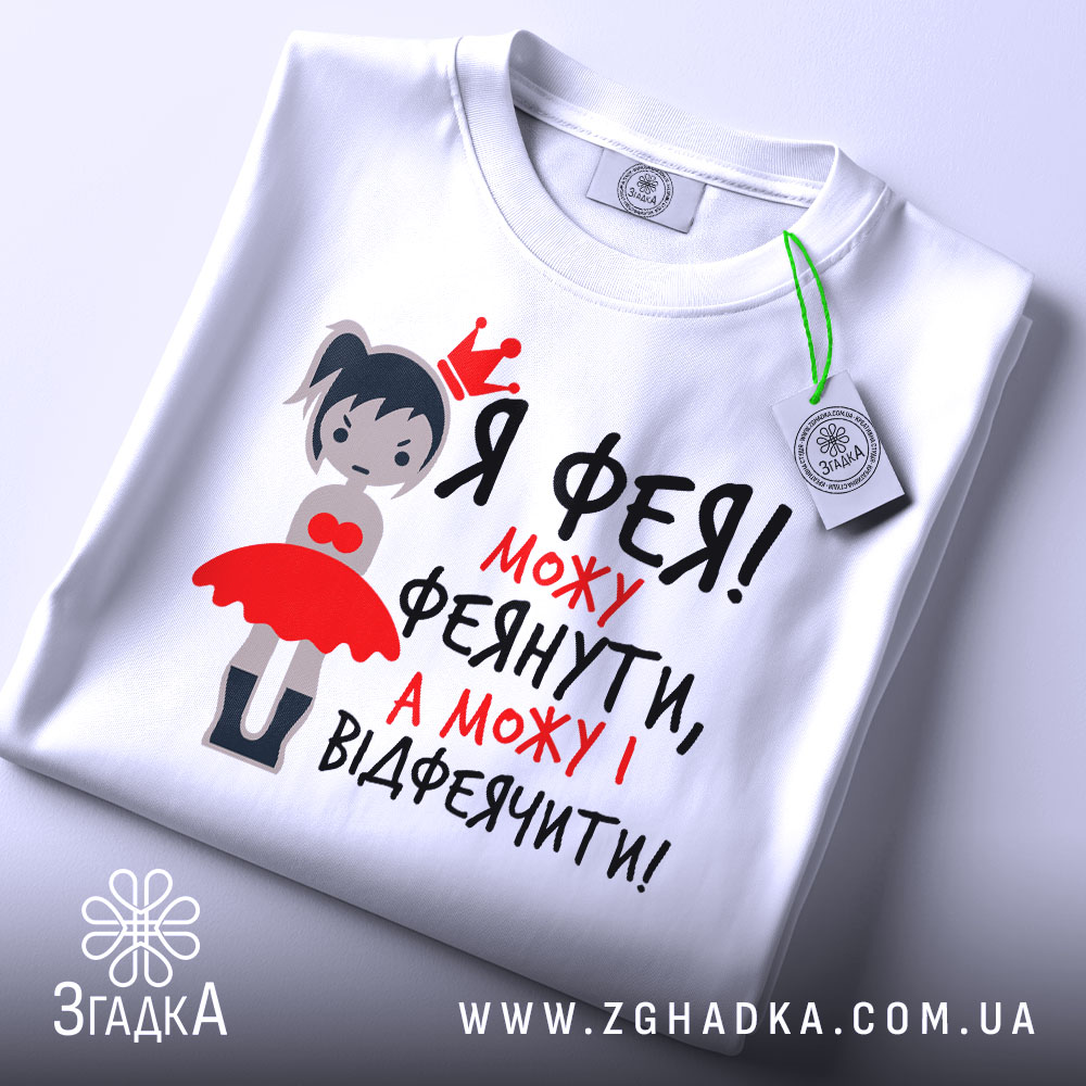 Футболка фея можу феянути, біла футболка на плоскій поверхні, з принтом дівчинки-феї в червоній сукні, текст чорного та червоного кольору, з етикеткою.