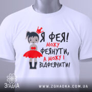 Футболка фея можу феянути, біла футболка на плоскій поверхні, з принтом дівчинки-феї в червоній сукні, текст чорного та червоного кольору, з етикеткою.